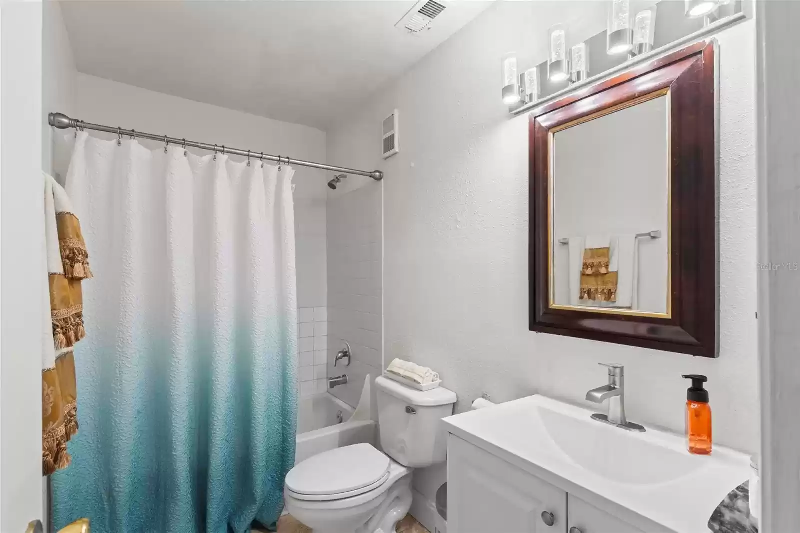 Second Bath Features a Tub with Shower,  Neutral Tile Flooring, a New Wood Vanity with a Stone Counter, Modern Brushed Chrome Mohen Faucet and New Chrome Artika 4 LED Light Fixture