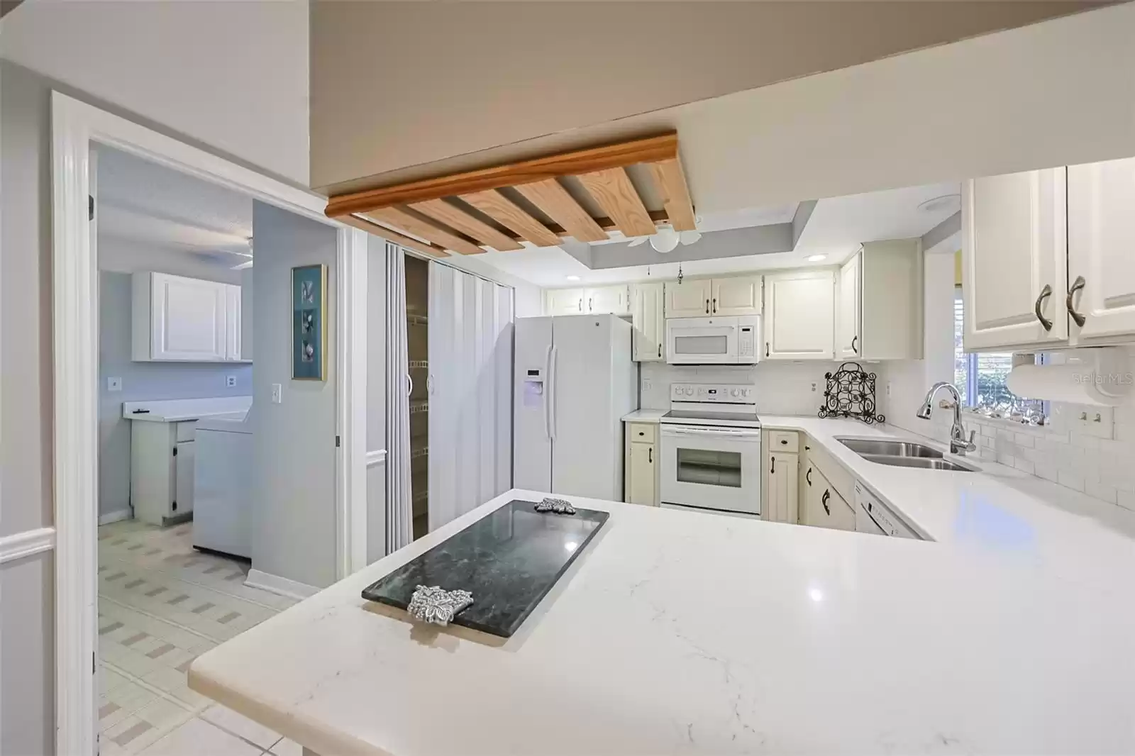 Kitchen allows for multiple cooks and is well equipped with dishes, cooking utensils, etc.  The view from the kitchen sink ensures that you never feel 'enclosed'.  Notice the kitchen also connects to the large separate indoor laundry room. Includes a wine rack and is lined with a subway tile backsplash. Recessed lighting adds for additional brightness. Includes pantry and undermount sink overlooking the Florida room.