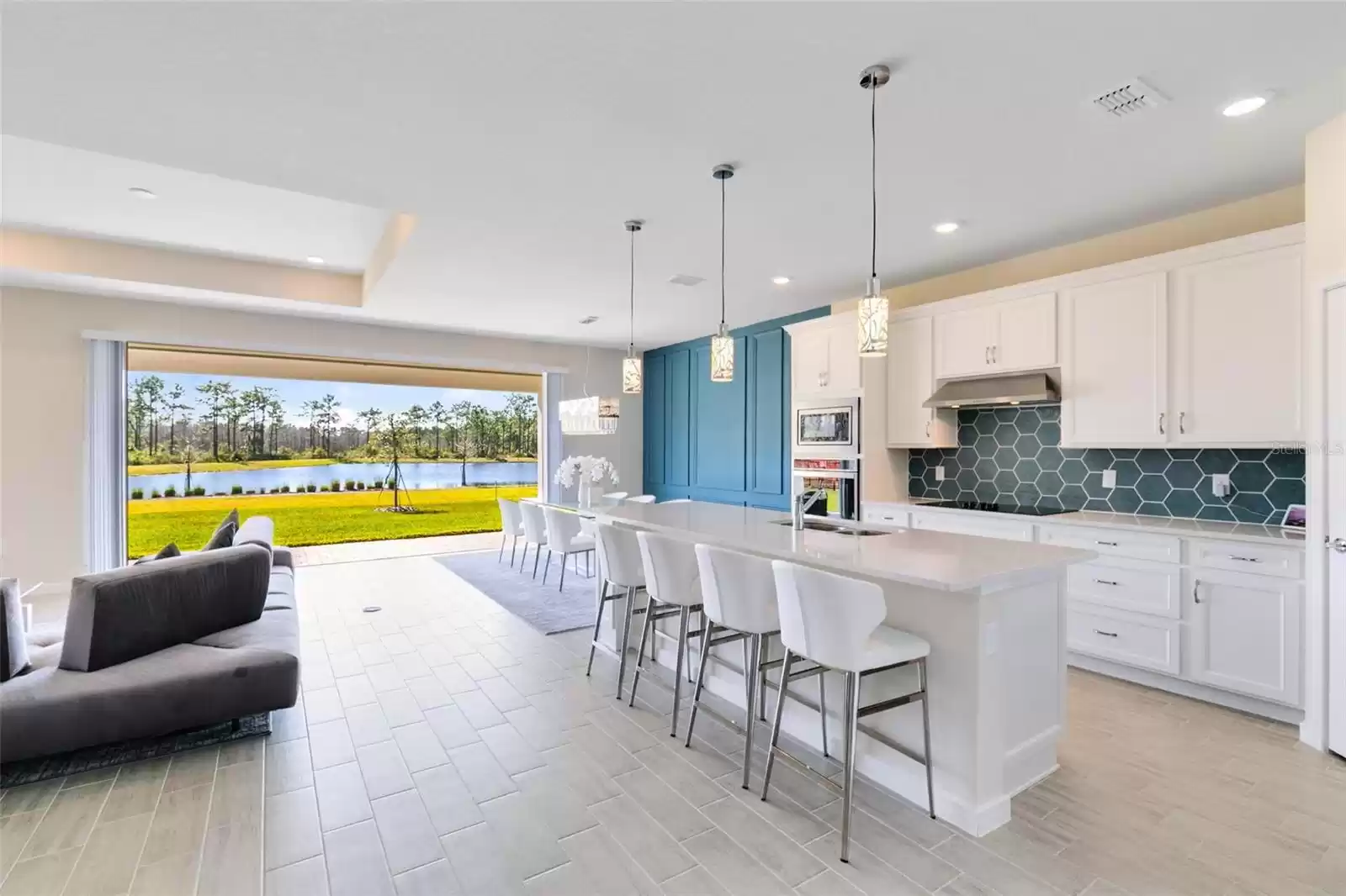 View of open living room/kitchen with quadruple sliders open to the pond view.