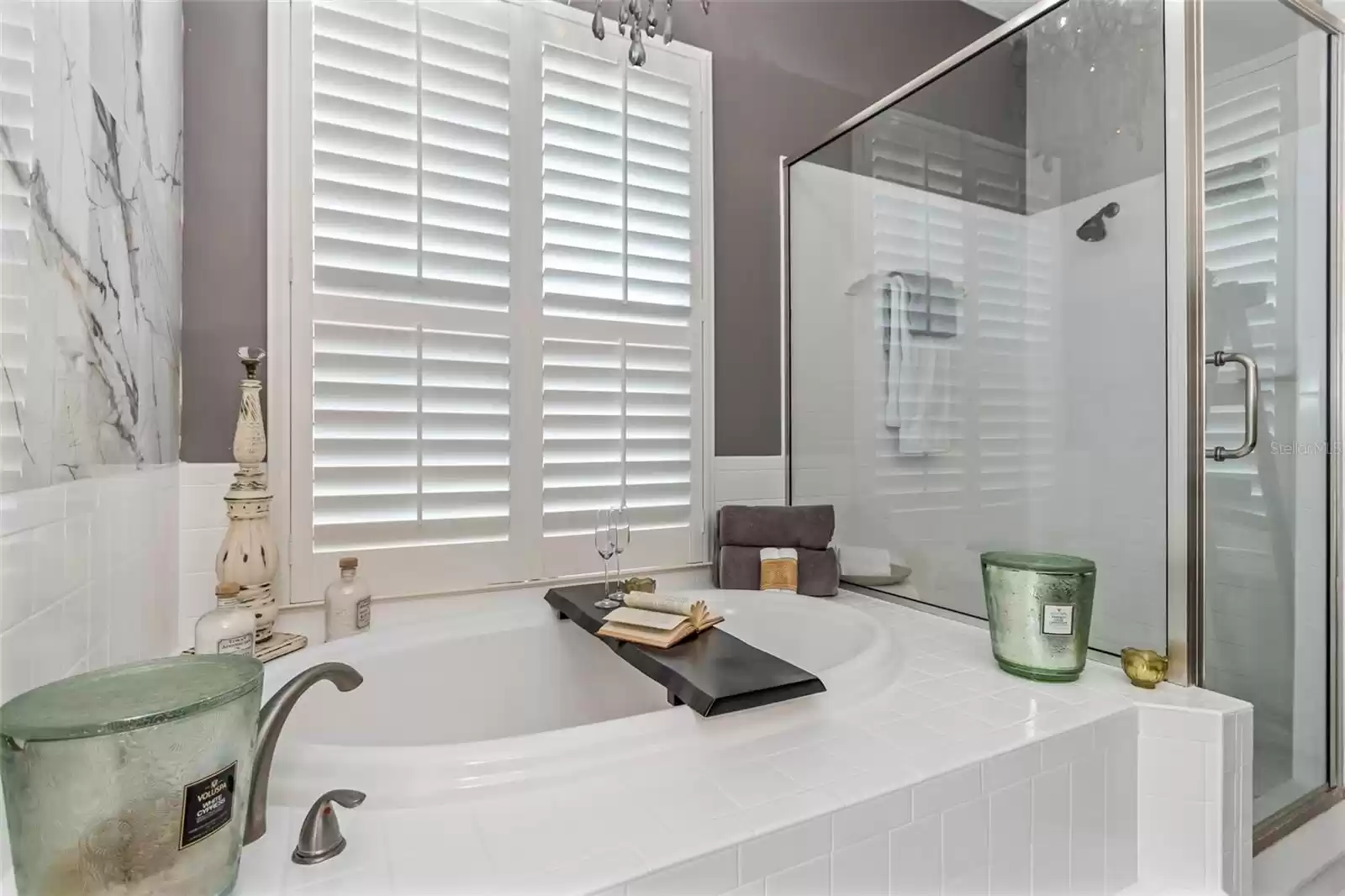 View of primary bathroom garden tub with plantation shutters and separate walk-in shower