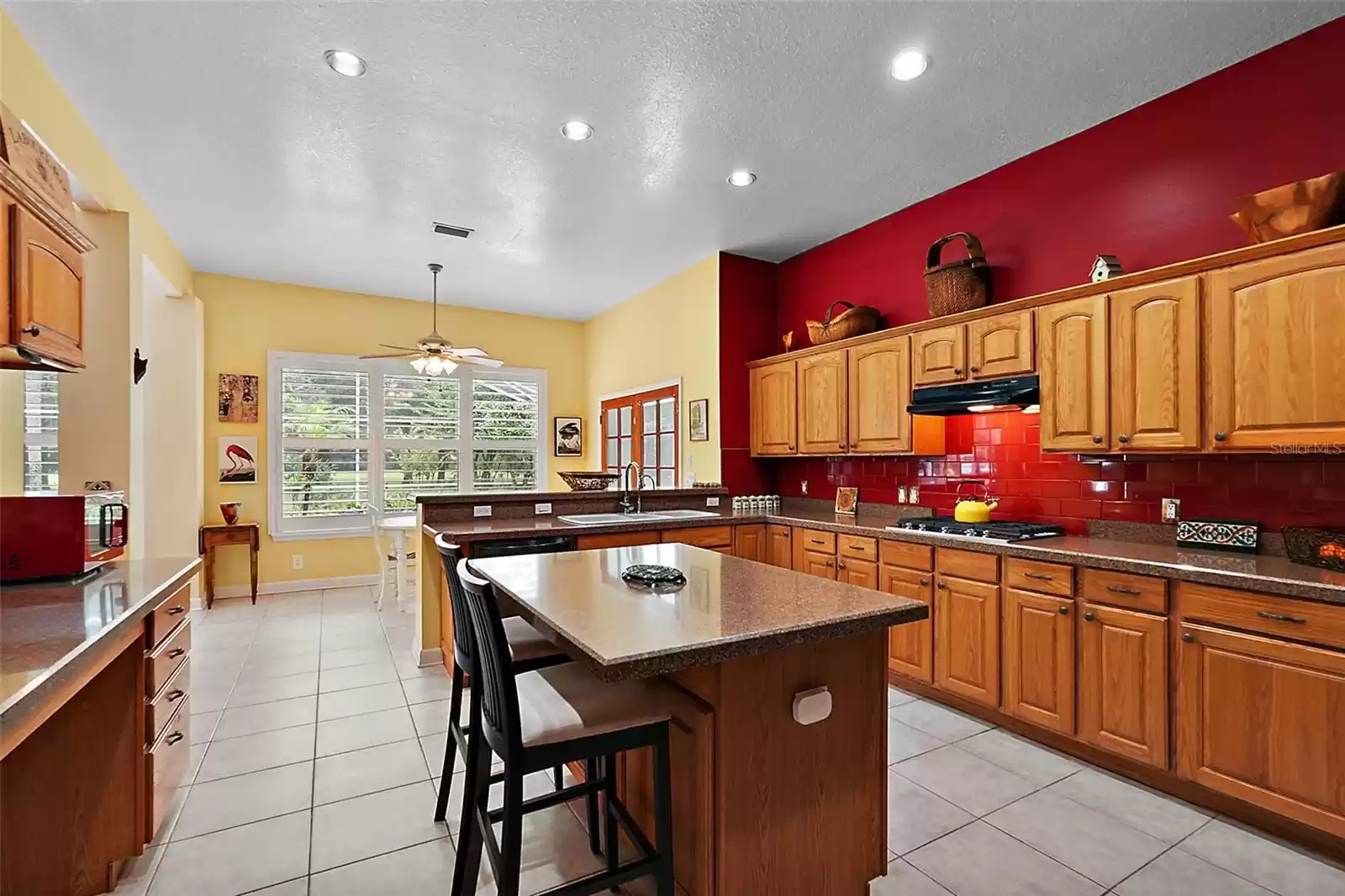 This spacious kitchen exudes warmth and style with its vibrant red tile backsplash, which adds a bold pop of color against the natural oak wood cabinetry.