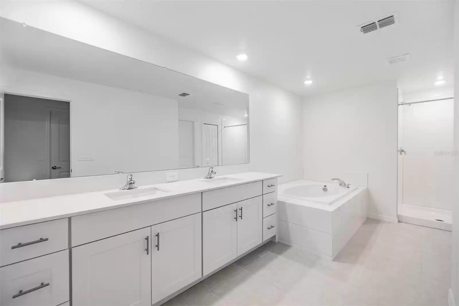 Dual square undermount sinks in quartz counters with stainless pulls, separate shower andsoaking tub in Primary bath ensuite